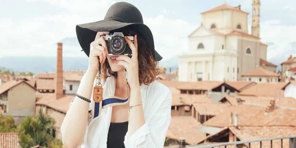 gadis cantik pakai topi sedang menggunakan kamera untuk foto pemandangan desa